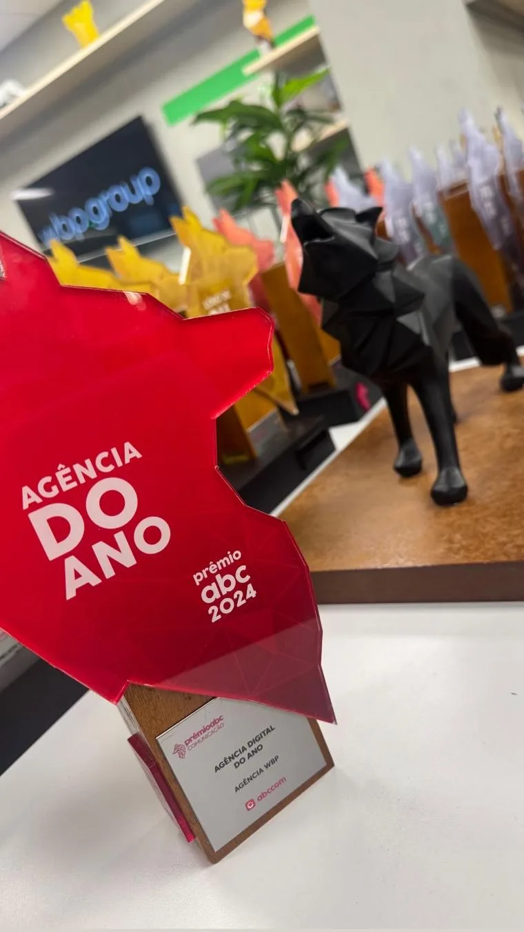 Placa vermelha Agência do Ano do Prêmio ABC 2024, gravada “Agência Digital do Ano” com o nome da agência abaixo, diante da mesa de troféus