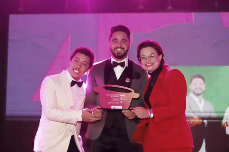 Alex Pinhol de smoking recebendo no palco a placa de Melhores Práticas de Mercado do Prêmio ABC da Comunicação